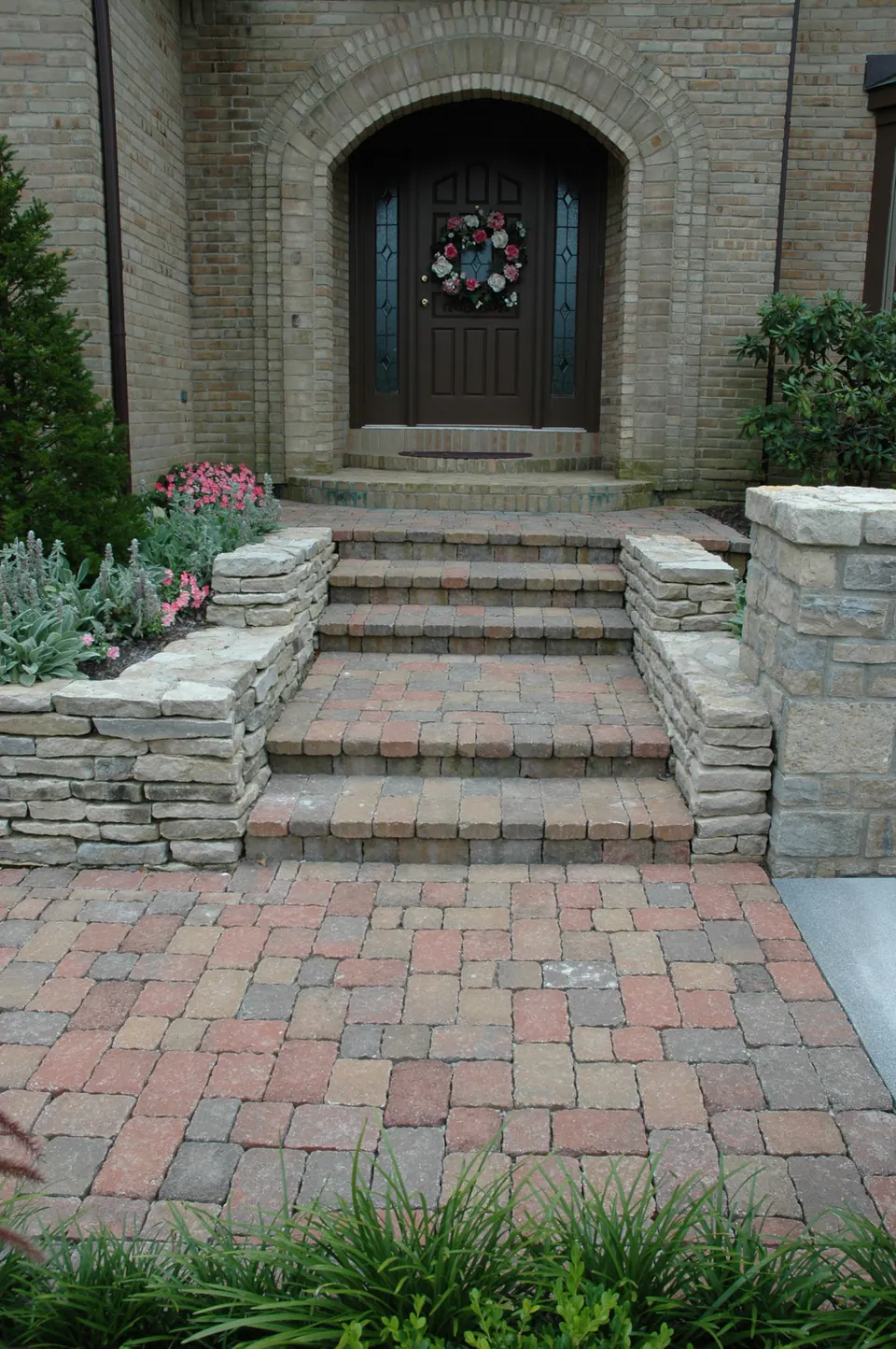 Low stone walls framing paver steps up to an arched front door
